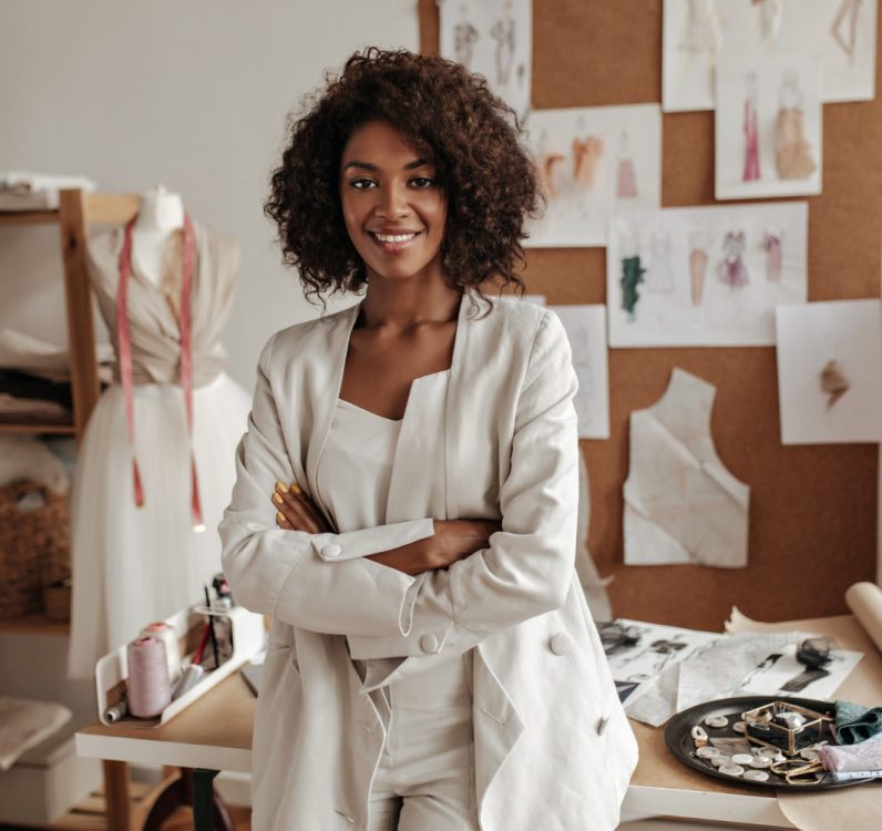 beautiful-curly-brunette-dark-skinned-fashion-designer-poses-office-leans-table